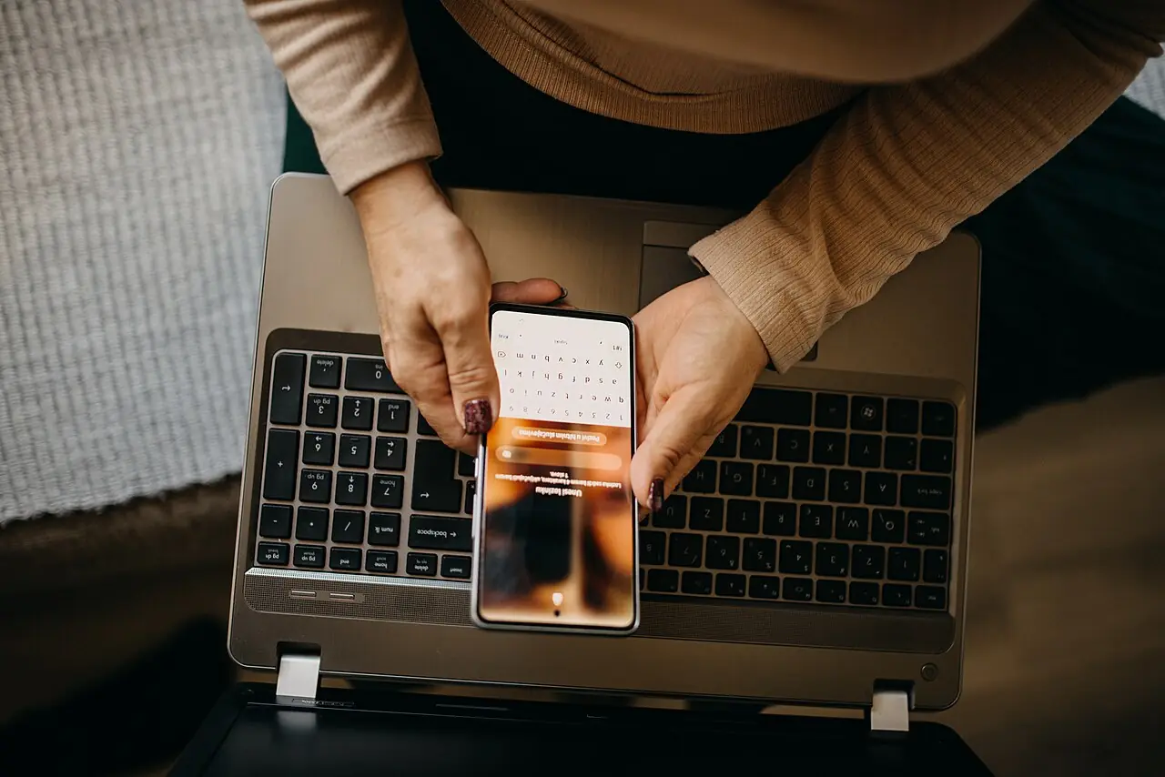Wanita menggunakan smartphone bersama laptop di atas meja